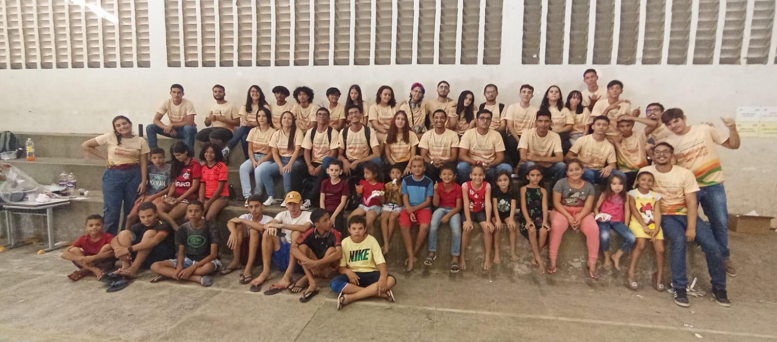 Se ve a un grupo de gente, mayor y niños y niñas, delante de una casa o edificio mirando a cámara