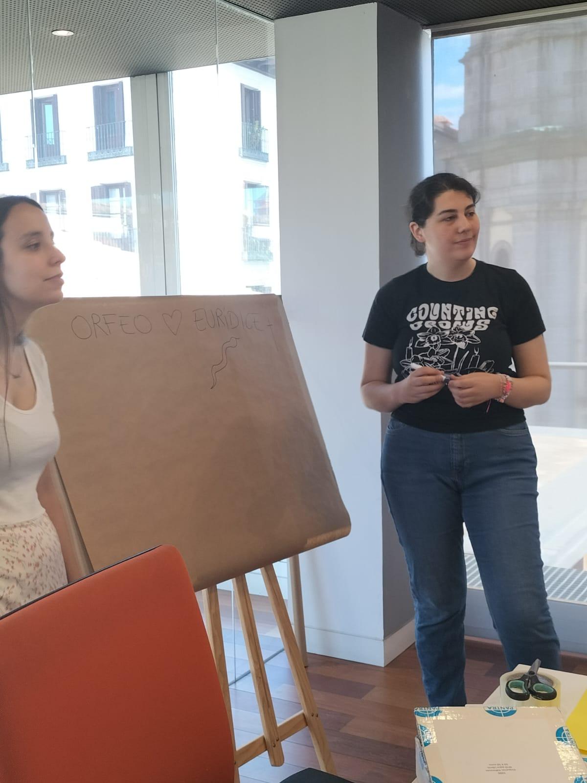 se ve una pizarra de papel en medio y dos personas una a cada lado, que son estudiantes UCM impartiendo el taller